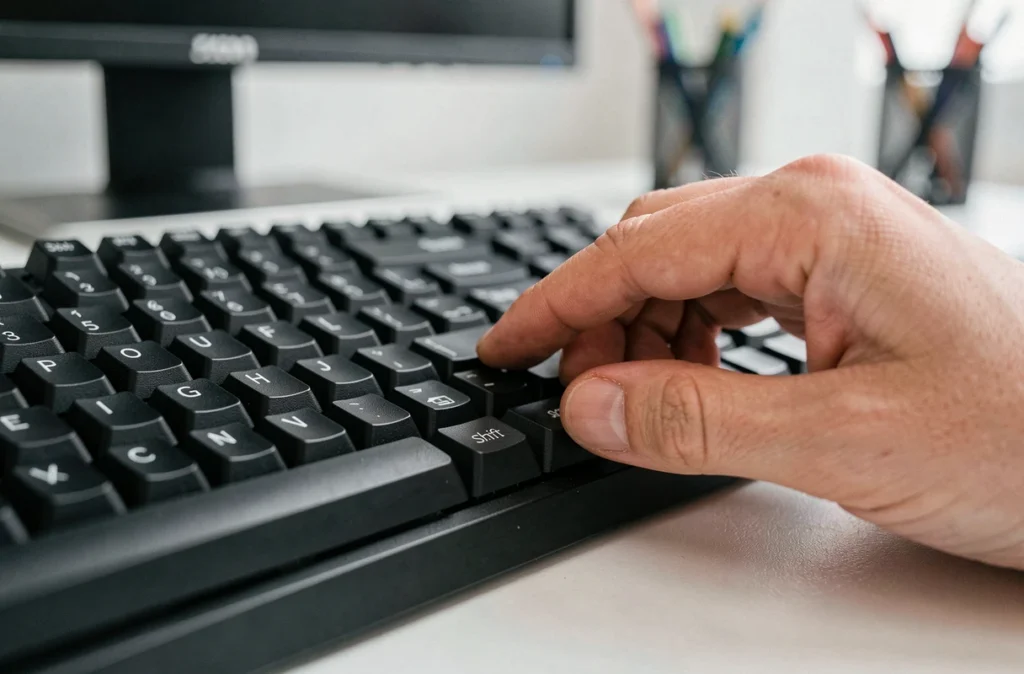 Gros plan sur la touche Shift d'un clavier mécanique noir avec une main appuyant dessus sur un bureau blanc épuré